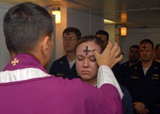 During the Ash Wednesday ceremony, a priest marks a woman's forehead with ash, while several people stand behind her, participating in this sacred occasion.